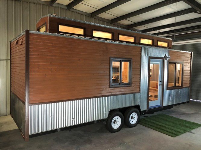 External view of this tiny home on wheels, showing 8 windows and the windowed front door.