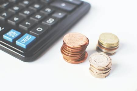 A stack of British coins alongside a calculator in the background. From Breakingpic at Pexels.com