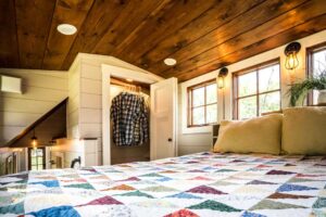 Timbercraft Tiny Homes' Denali gooseneck tiny house; a look at the master bedroom with a double bed and in-built storage via a wardrobe.
